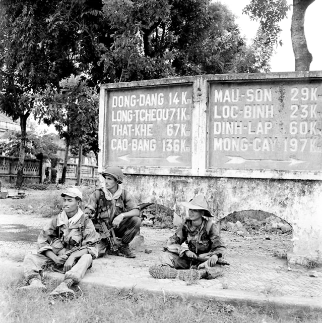 two soldiers are sitting on the ground beside the sign