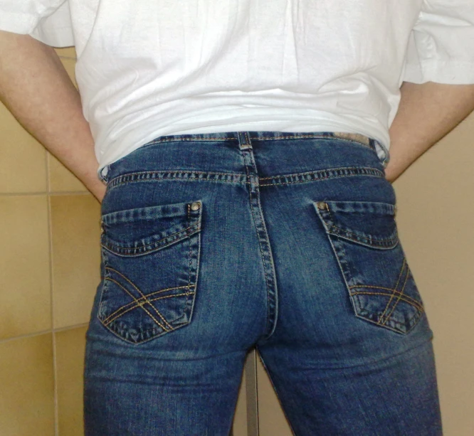 man standing in front of a brown tile wall wearing his jeans
