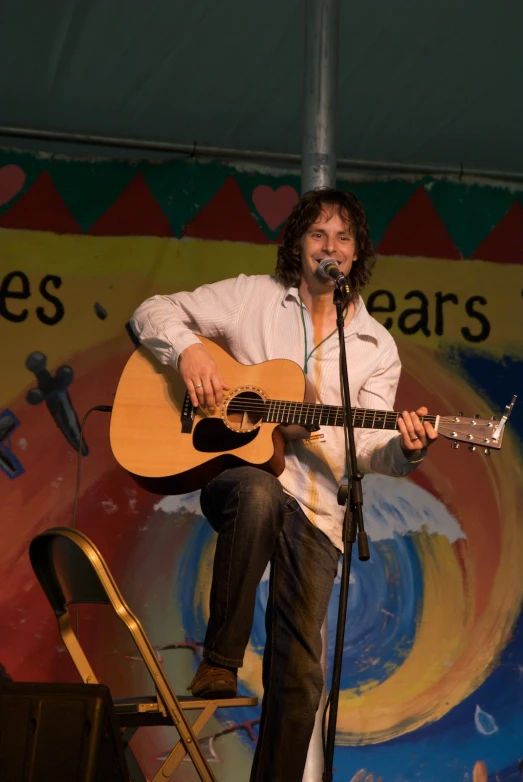 man holding guitar while performing with a microphone and large wall