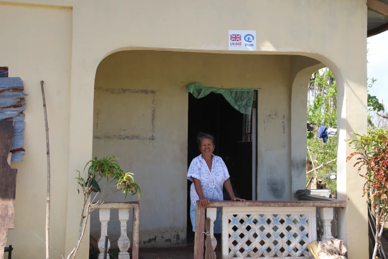 an elderly person stands at the entrance of a beige house