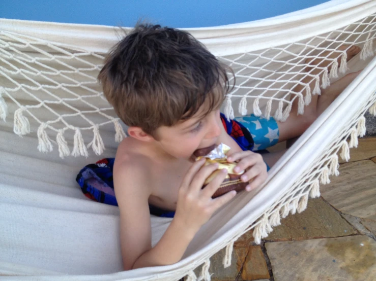 a  laying in a hammock eating a sandwich