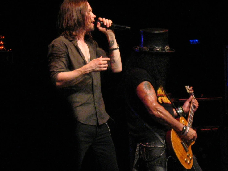 two guys performing on stage with one holding a guitar and the other holding a microphone
