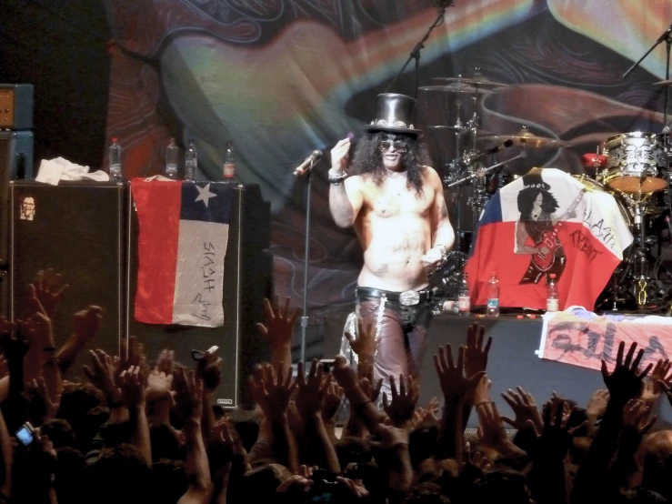 a man in a silver top standing on a stage with one arm raised