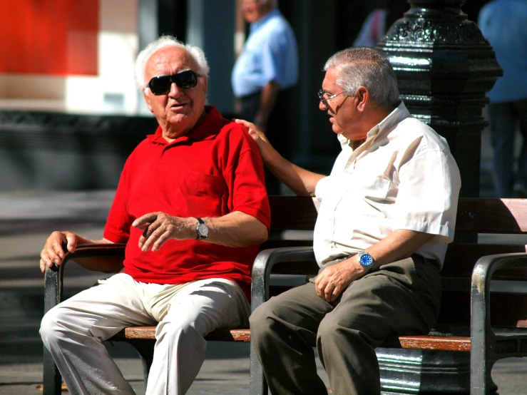 two older men sitting on a bench with one touching the other