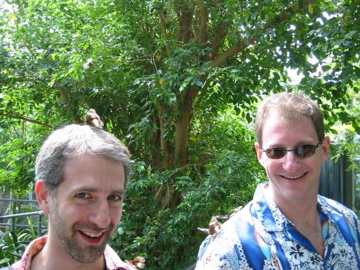 two men standing next to each other in front of trees