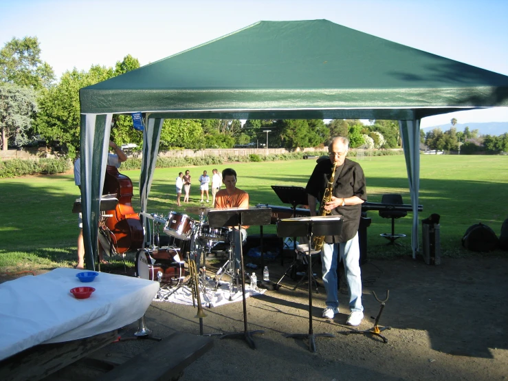 band on stage performing music under canopy and with trees in background