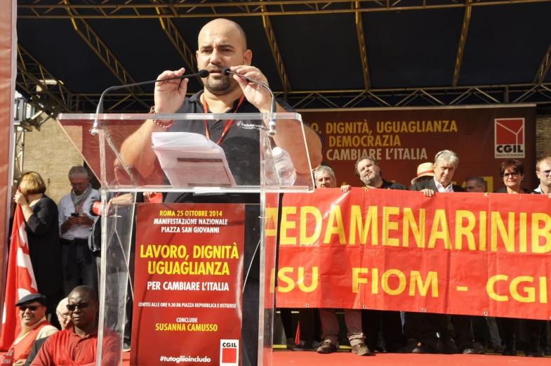 a man is speaking on stage as other people sit behind him