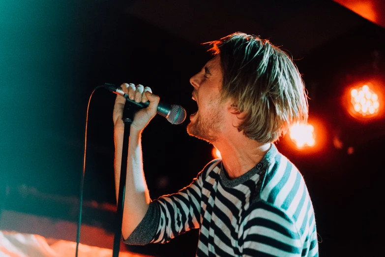 young adult male with dreadlocks holding a microphone and singing