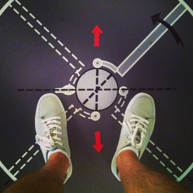 a close up image of a man's feet with white sneakers on standing in front of a line with arrows