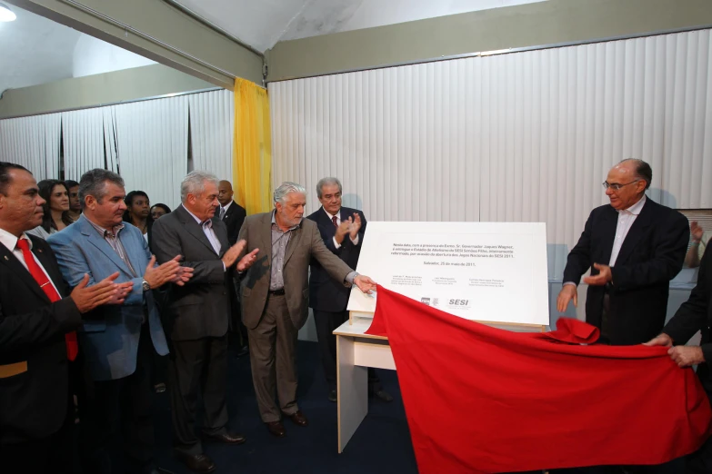 several men in suits and ties are standing around with one holding a red and white sign