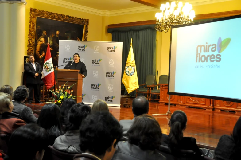 an audience watches as a speaker speaks to the press