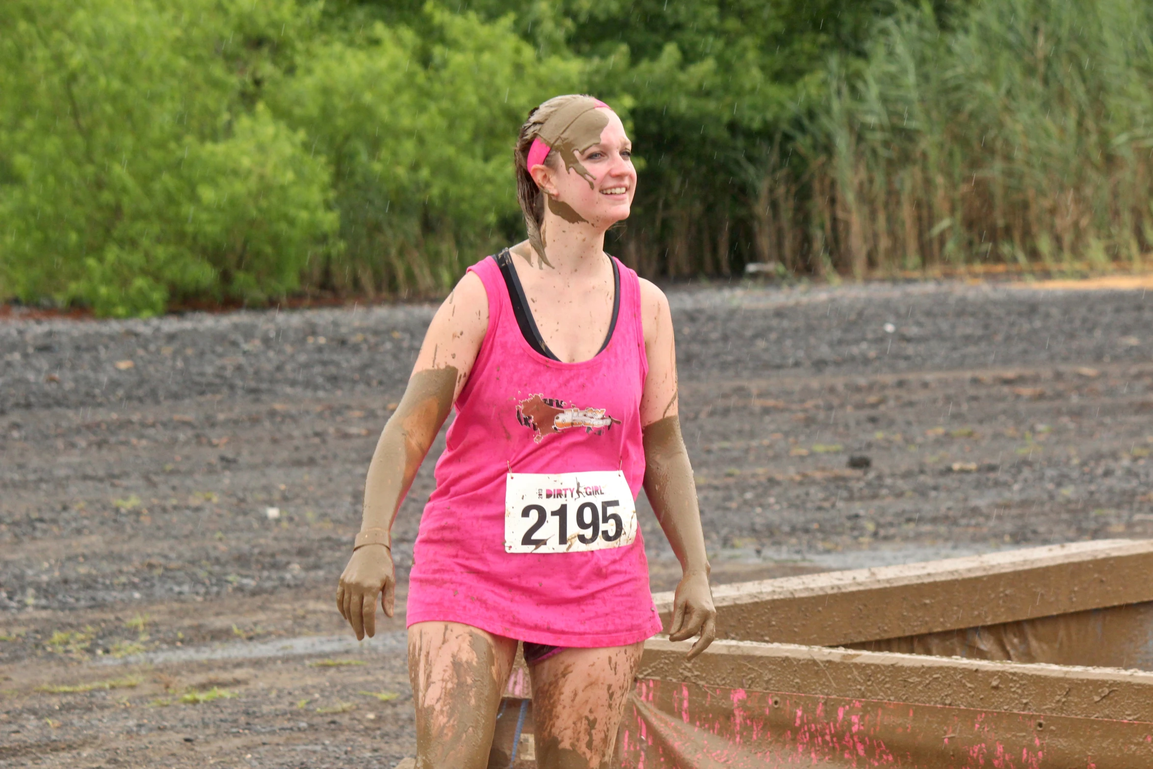 a young woman running on muddy ground with trees in the background