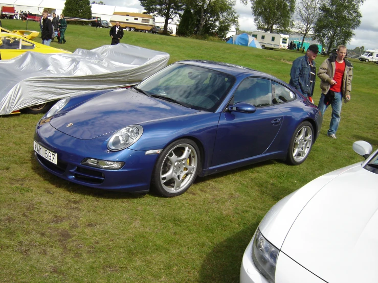 blue porsche coupe parked near many tents on the grass