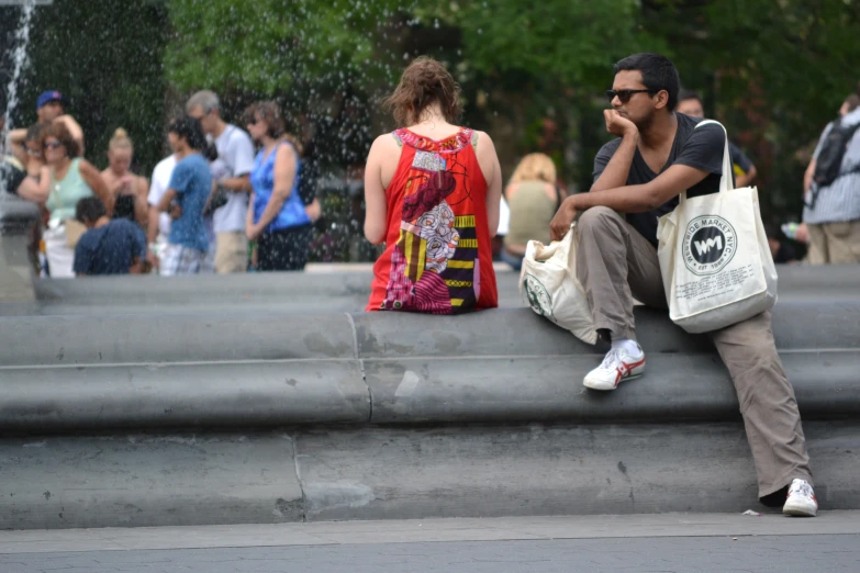 a man and woman sit on top of a fountain with others standing around