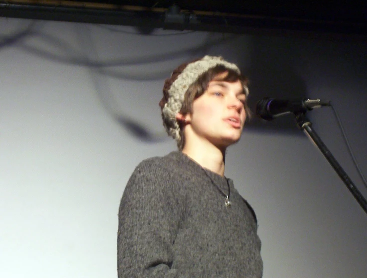 a woman standing next to a microphone with a knitted hat on