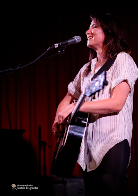 a woman playing a guitar while singing at a microphone