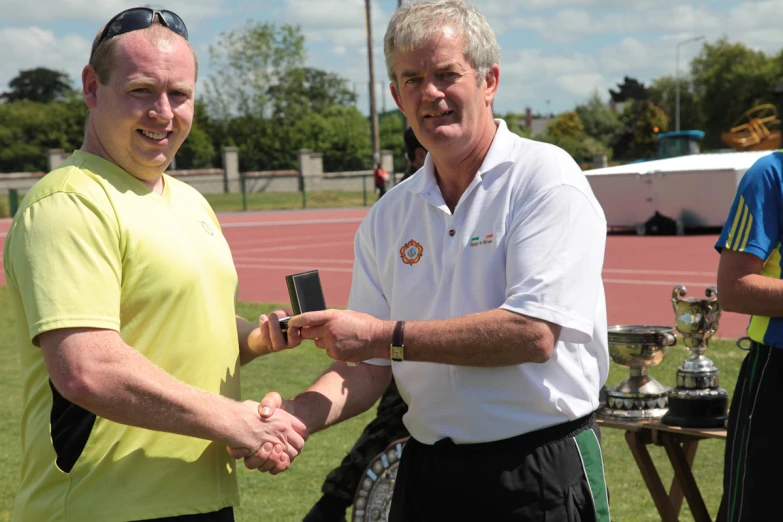 two men shaking hands over an award trophy