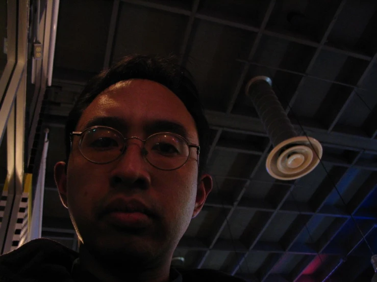 a man wearing glasses stands next to a ceiling fan