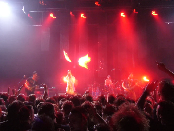 a concert with band members and fans in front of two large fire - lit screens