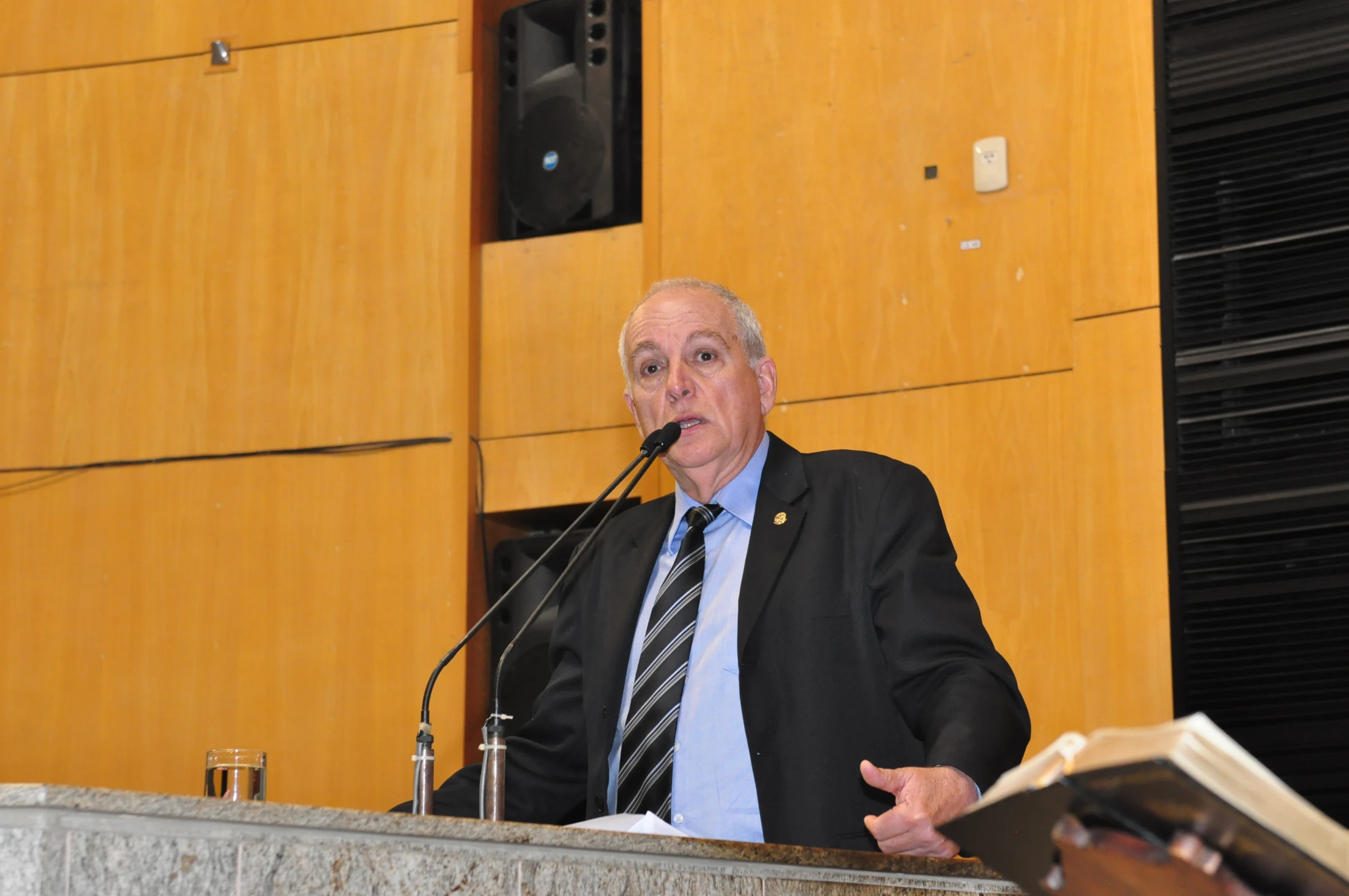 man at podium during speech in front of wood paneled wall