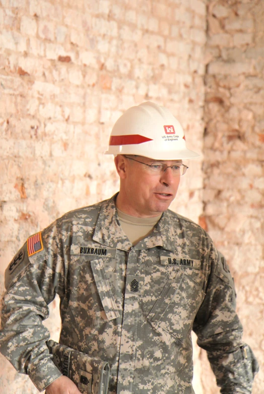 the man in uniform is standing near a brick wall