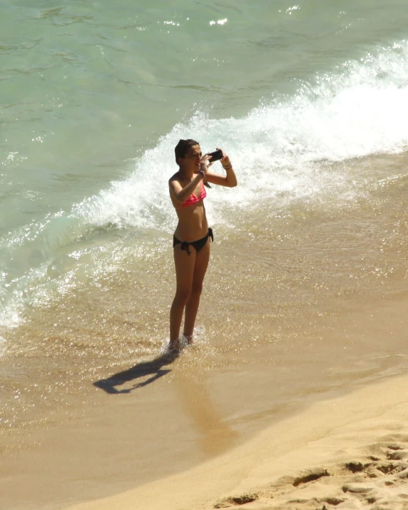 woman standing on beach and taking pos with cell phone
