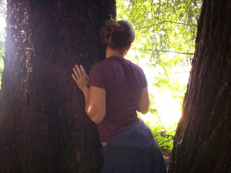 the woman is holding her hands together behind a tree