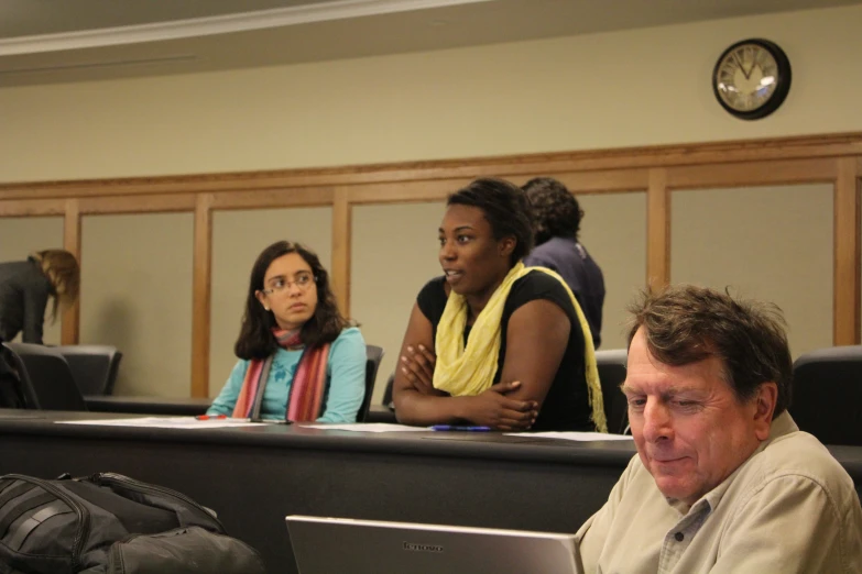 people sit around a lecture room with two men looking at a laptop