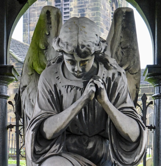 the statue is covered in gray paint, with wings and a ball at his hands