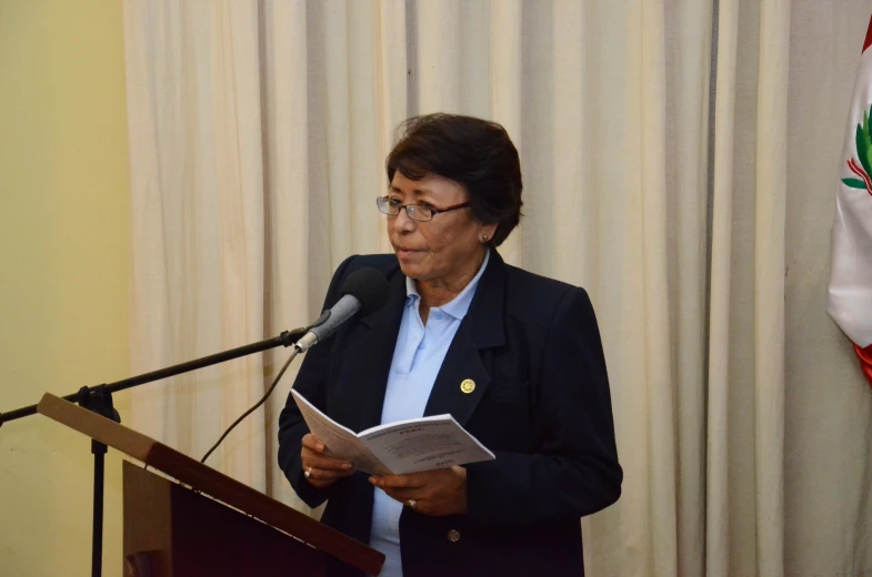 a woman in glasses standing behind a podium and reading