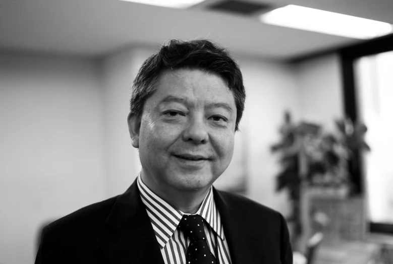 an asian man in suit and tie standing in front of some windows