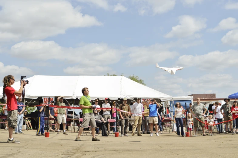 a crowd gathered around a tent watching a man fly an airplane