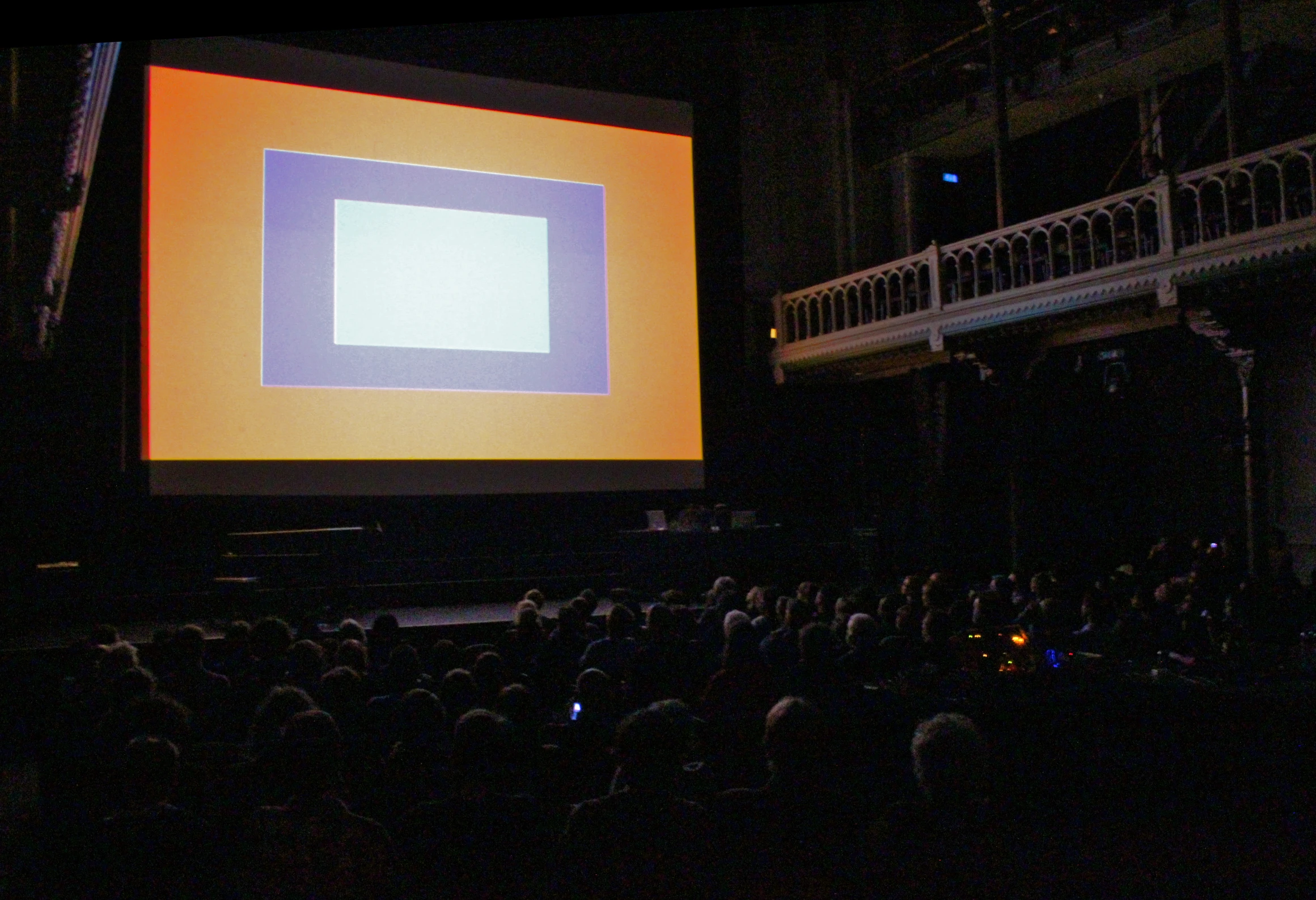 a large projection screen in front of an auditorium with people seated