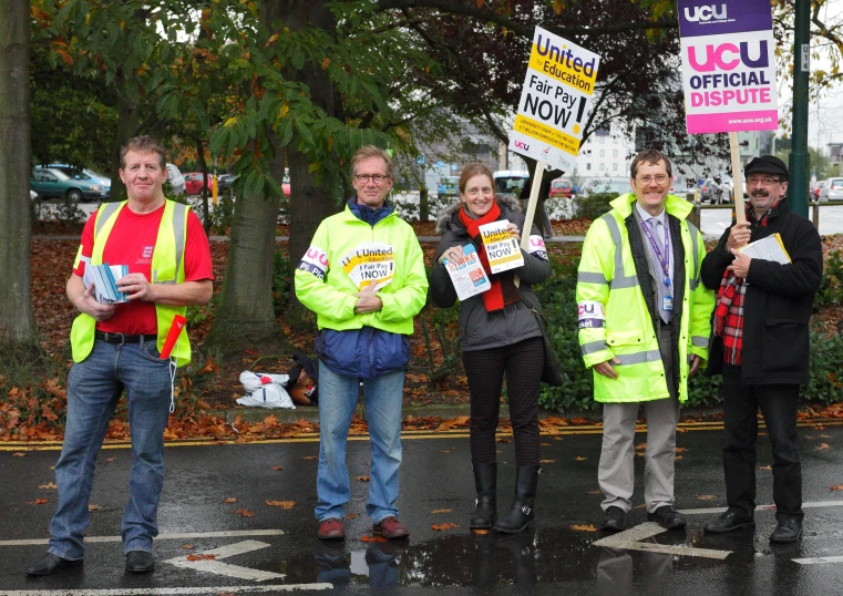 people in bright yellow vests stand on the corner of a street