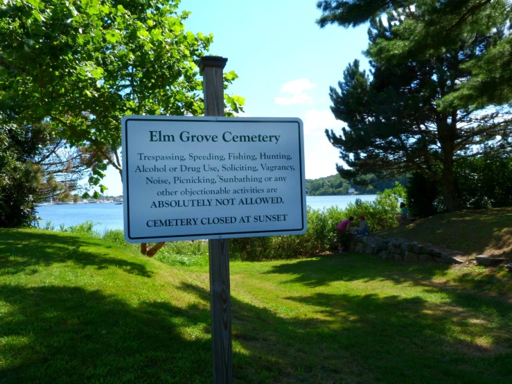 a sign on a post in a grassy field near the water