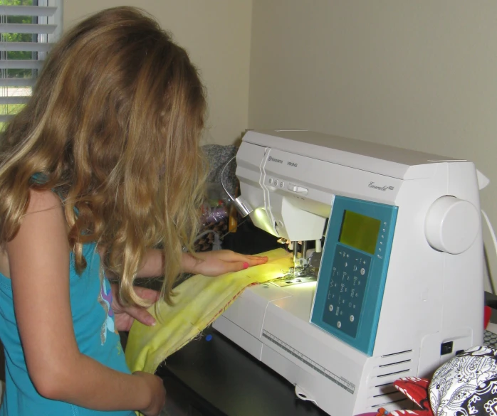 a girl holding a yellow cloth to an appliance on a sewing machine
