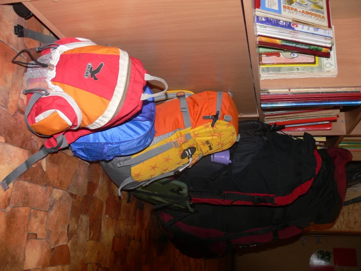 backpacks are lined up against the wall near book shelves