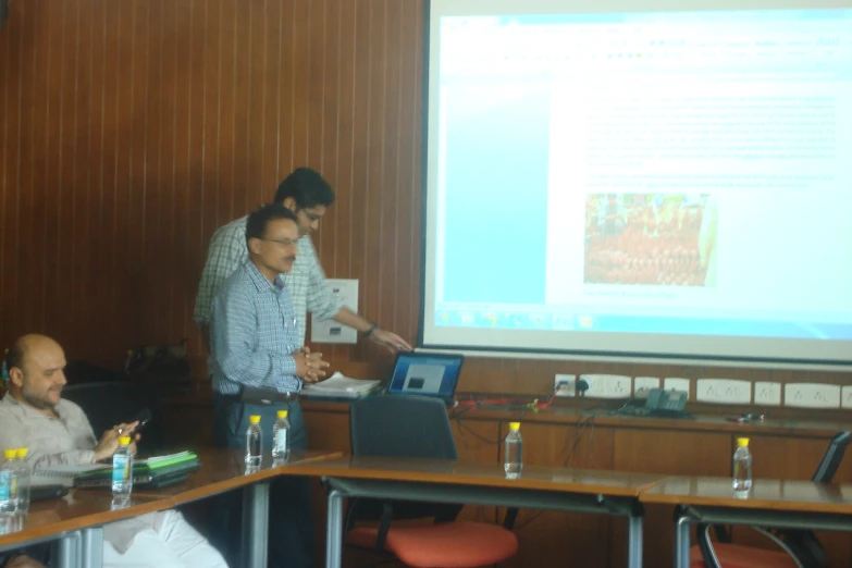 people standing in front of a presentation screen and two men on laptops