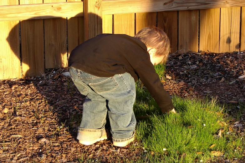 a boy bending over playing with some grass