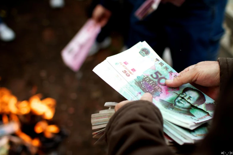 a person handing out money to someone near a campfire