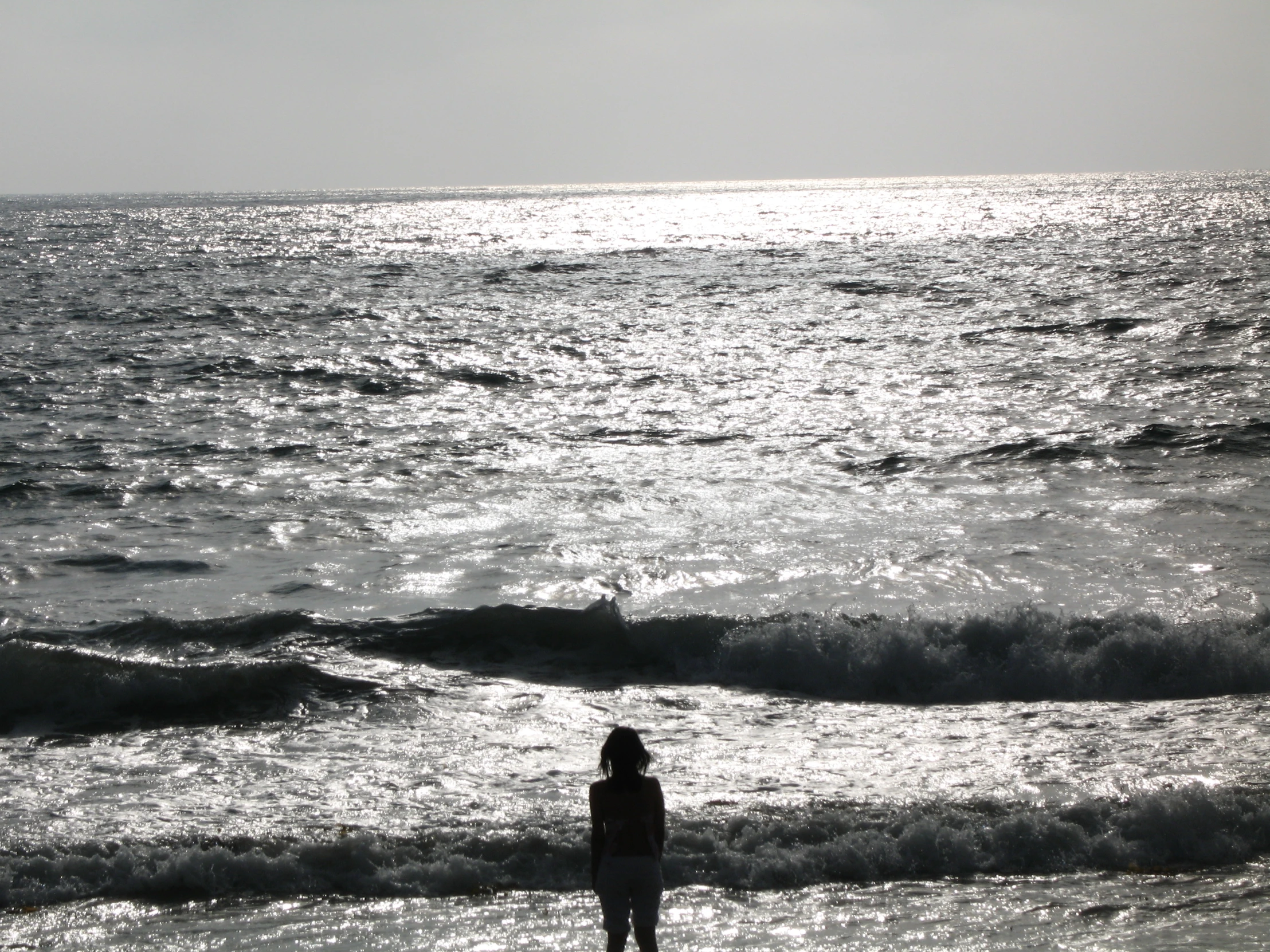 the woman is standing on the beach near the waves