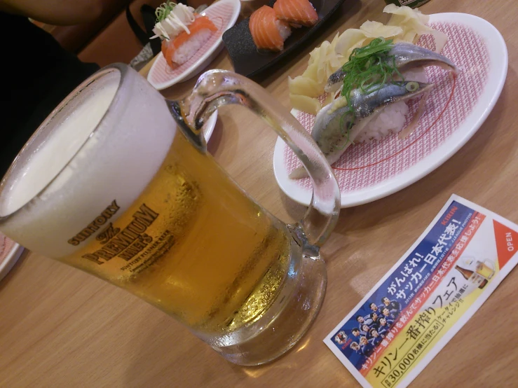 a cup of beer sitting next to a plate with sushi