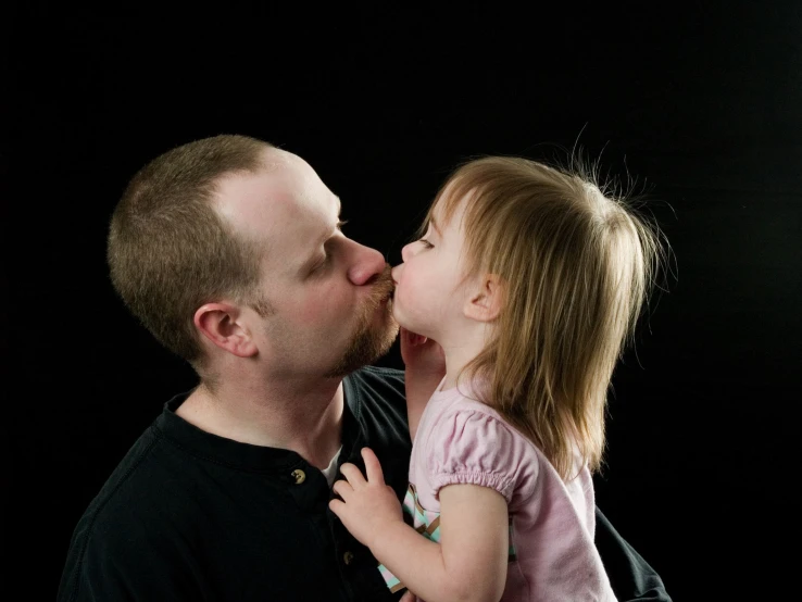 a man is kissing his little girl while she kisses her nose