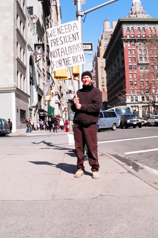 man holding a sign that reads we need a prestatuent loyallov for the rich