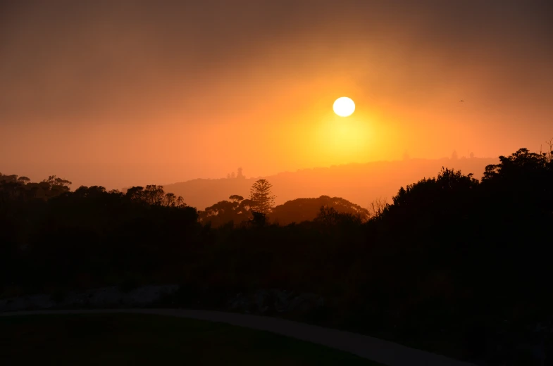 the sun sets over the mountains with trees and road winding in