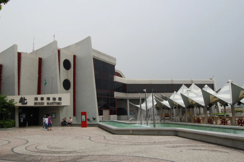 people are walking near the fountain in front of a large building