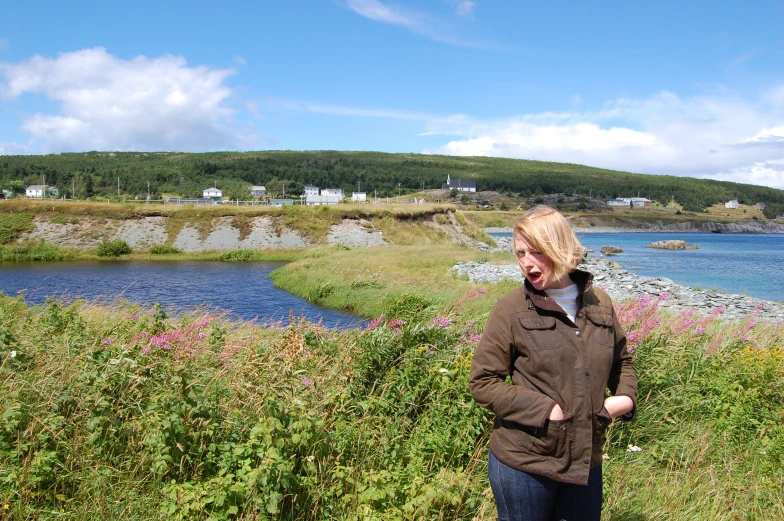 a woman stands near water on a hill