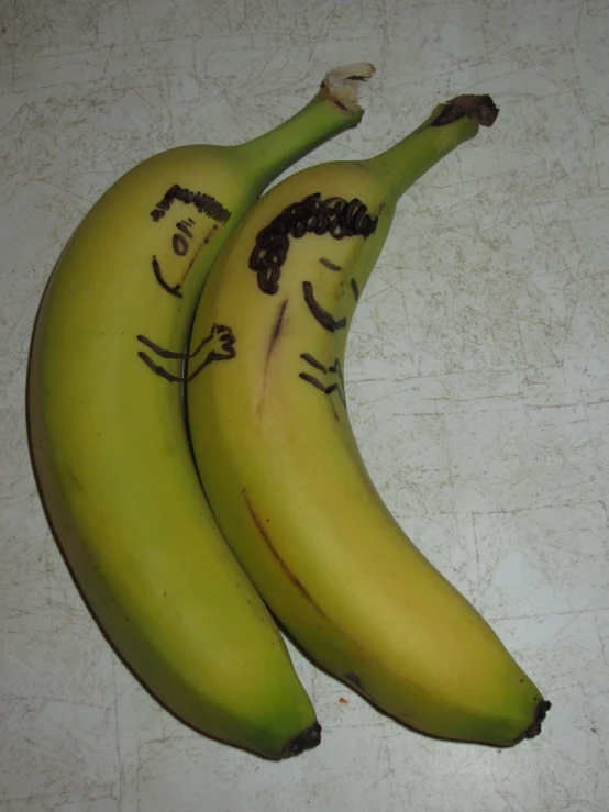 two ripe bananas on a white table one with writing