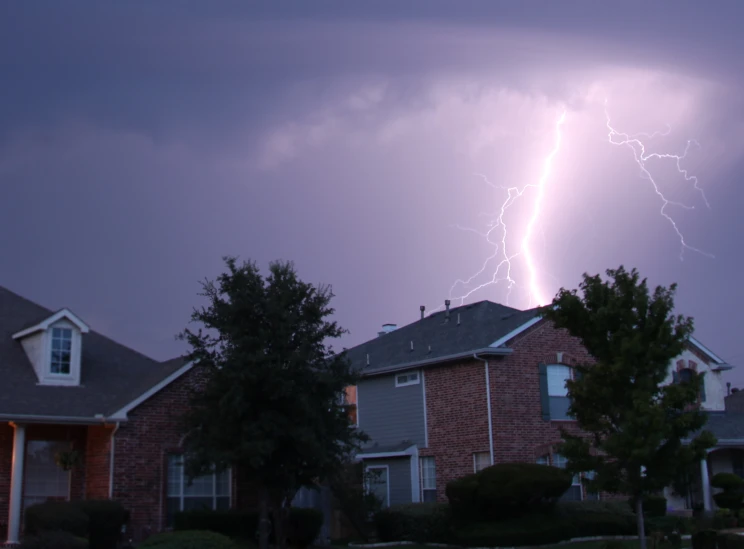 a lightning bolt strikes behind some houses on a cloudy night