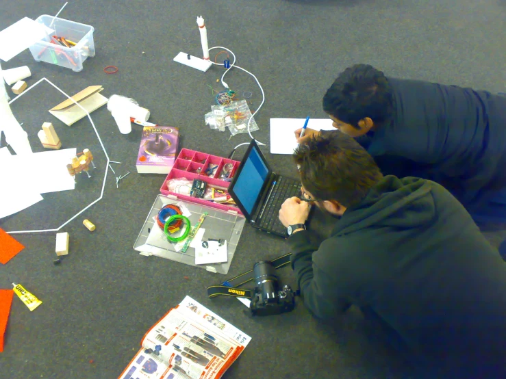 two men sitting on the floor with a laptop computer